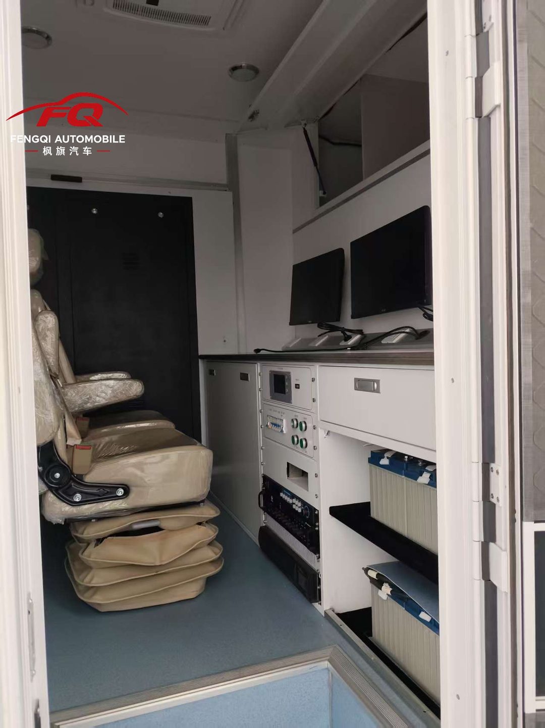 Battery bank installed on low racks beside the crew seats inside a command vehicle — heavy items sit below and beside the working area