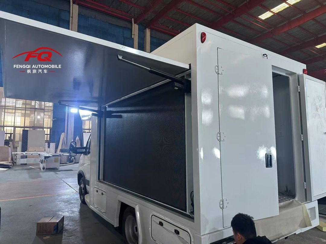 Folding LED screen mounted on the outside of a command vehicle body, held on hydraulic struts — a large load carried high and outboard